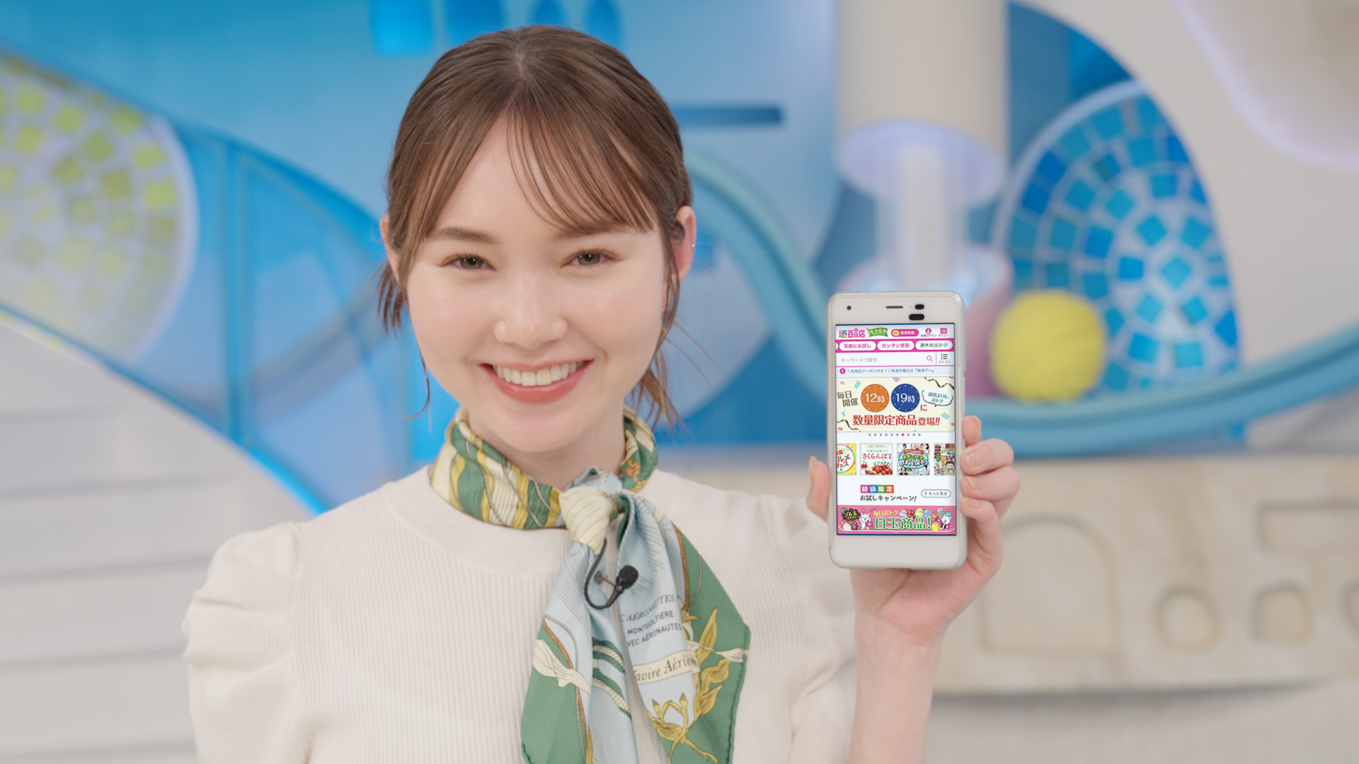 左手にスマホを持ち笑顔でスマホ画面をこちらに見せているマーシュ綾さん。スマホ画面にはサンプル百貨店サイトが表示されている。